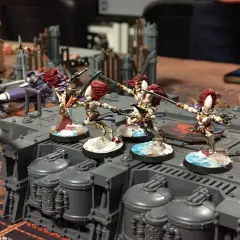 Figurki wojowniczek Eldarów, jednej z frakcji Warhammer 40k, szykują się do walki na szarej platformie.