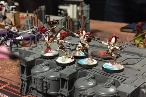 Figurki wojowniczek Eldarów, jednej z frakcji Warhammer 40k, szykują się do walki na szarej platformie.