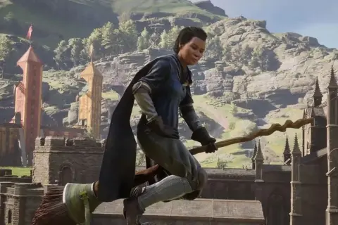 Gracz na miotle w grze Hogwarts Legacy Quidditch, lecący nad zamkiem i górami.