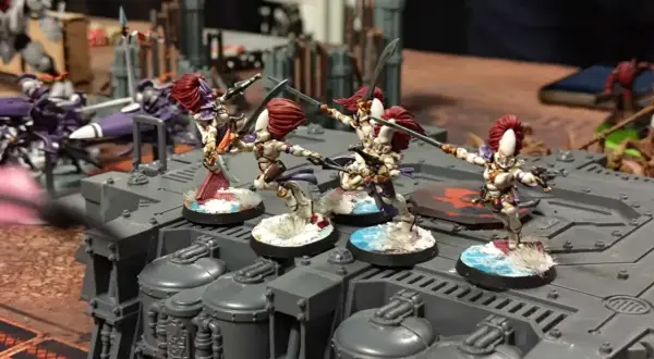 Figurki wojowniczek Eldarów, jednej z frakcji Warhammer 40k, szykują się do walki na szarej platformie.