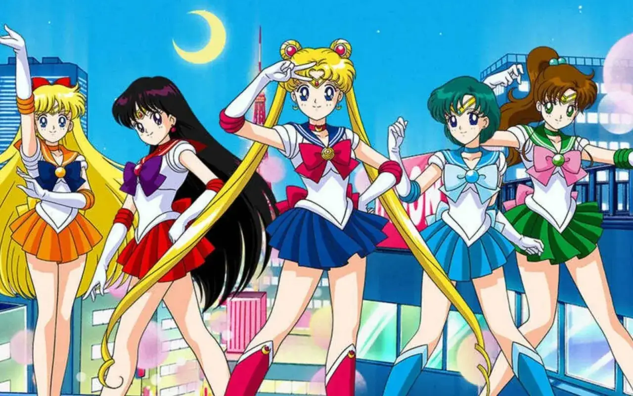 Pięć wojowniczek Sailor Moon w swoich charakterystycznych strojach pozuje na tle nocnego miasta.