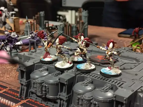 Figurki wojowniczek Eldarów, jednej z frakcji Warhammer 40k, szykują się do walki na szarej platformie.
